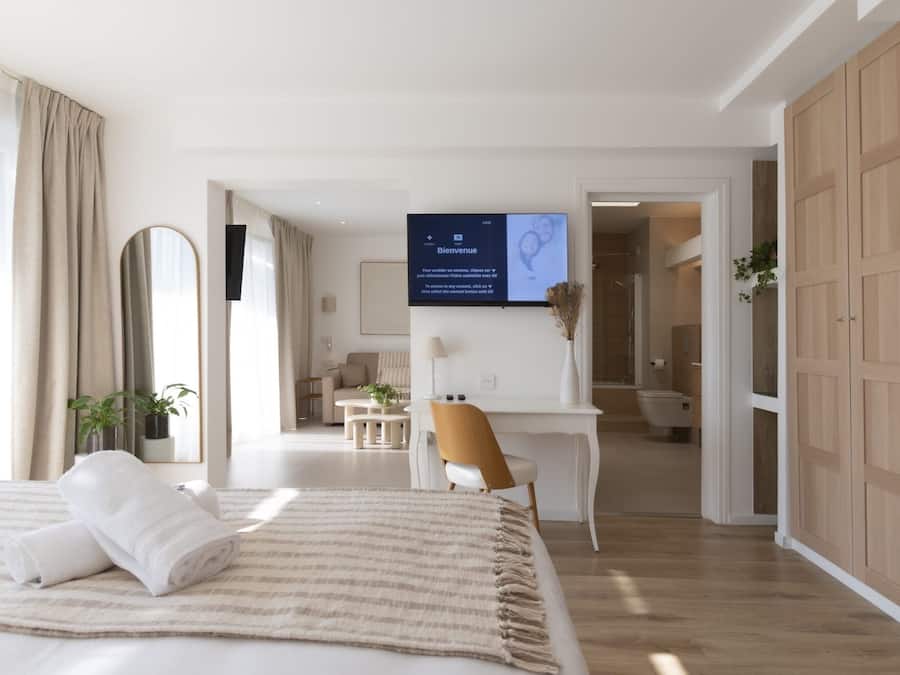 A modern hotel room with a bed, a desk, and a TV displaying a welcome message.