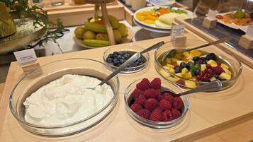 A buffet with various food items including yogurt, blueberries, raspberries, and a fruit salad.