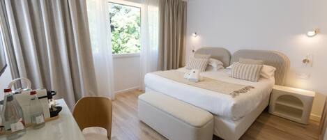 Habitación de hotel con una cama grande, mesitas de noche, una silla, un escritorio con artículos de tocador y una ventana con cortinas.