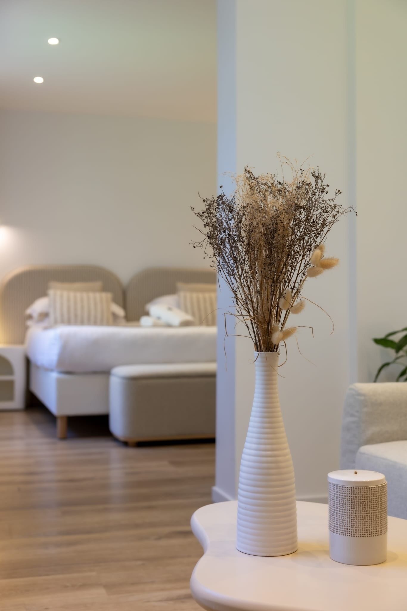 A modern bedroom with a bed, bedside table, and a vase with dried flowers.