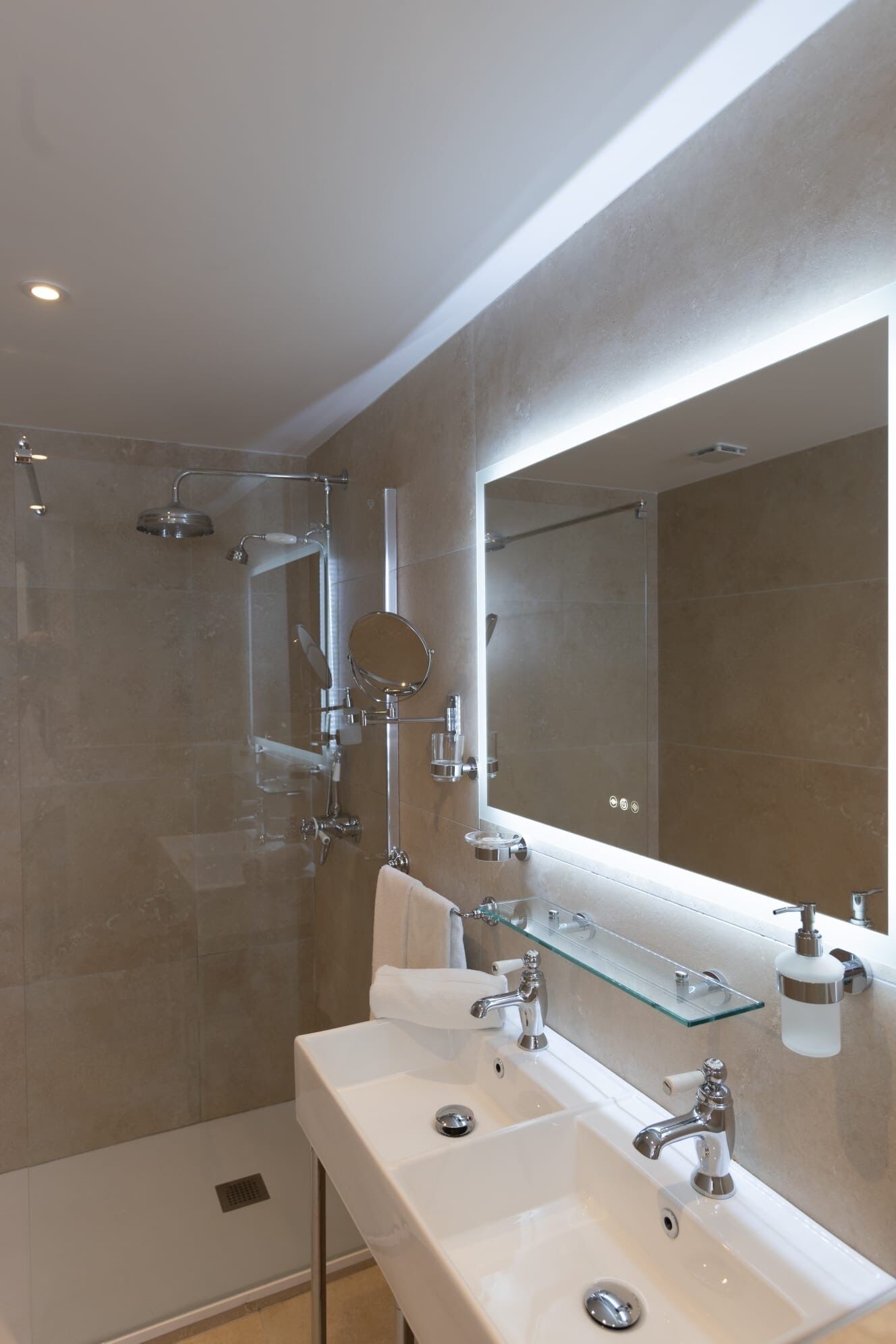 Un baño moderno con cabina de ducha de vidrio, un espejo grande y dos lavamanos con grifería cromada.