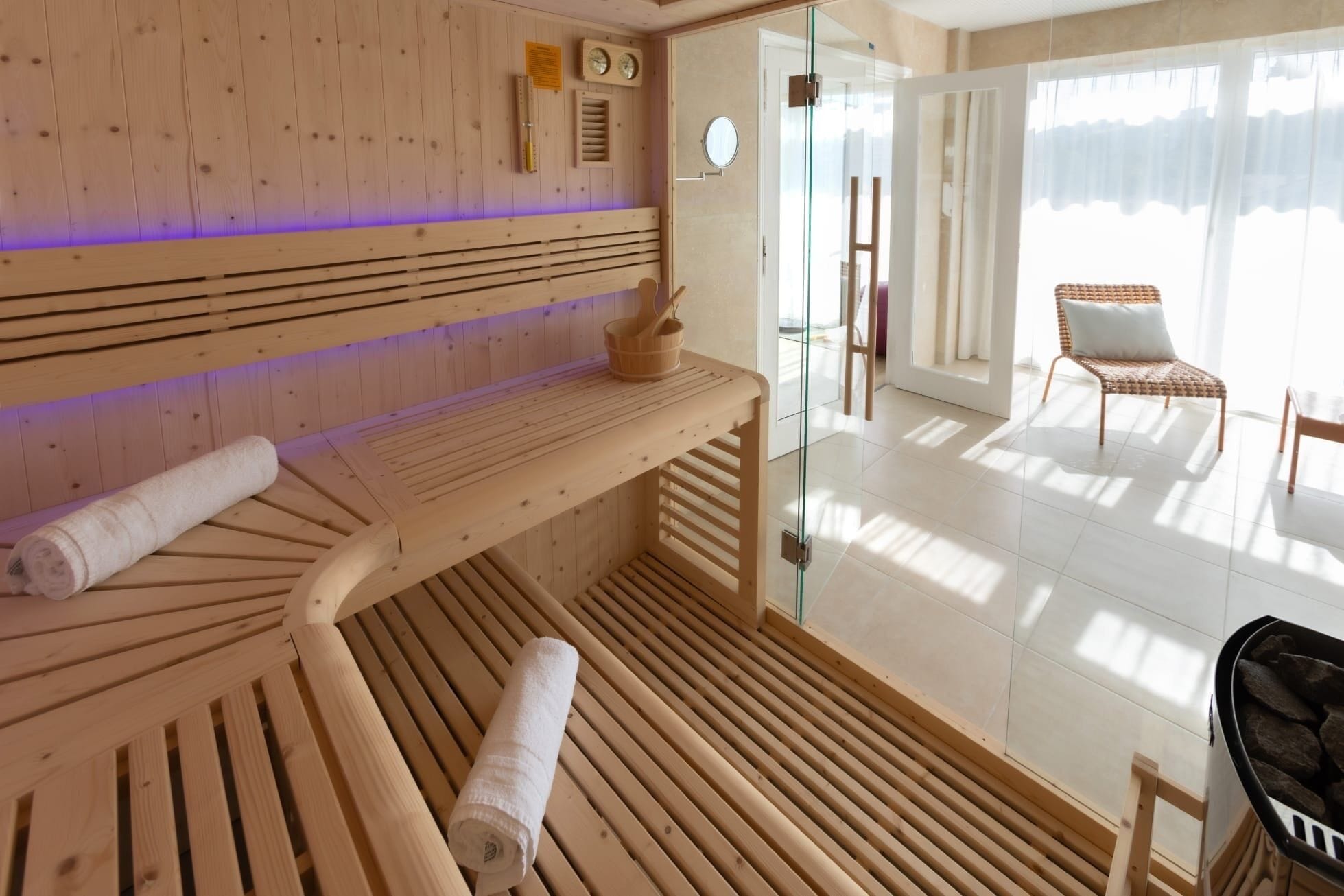 Un sauna avec des bancs en bois, une porte en verre donnant sur l’extérieur et une vue sur l’espace extérieur.