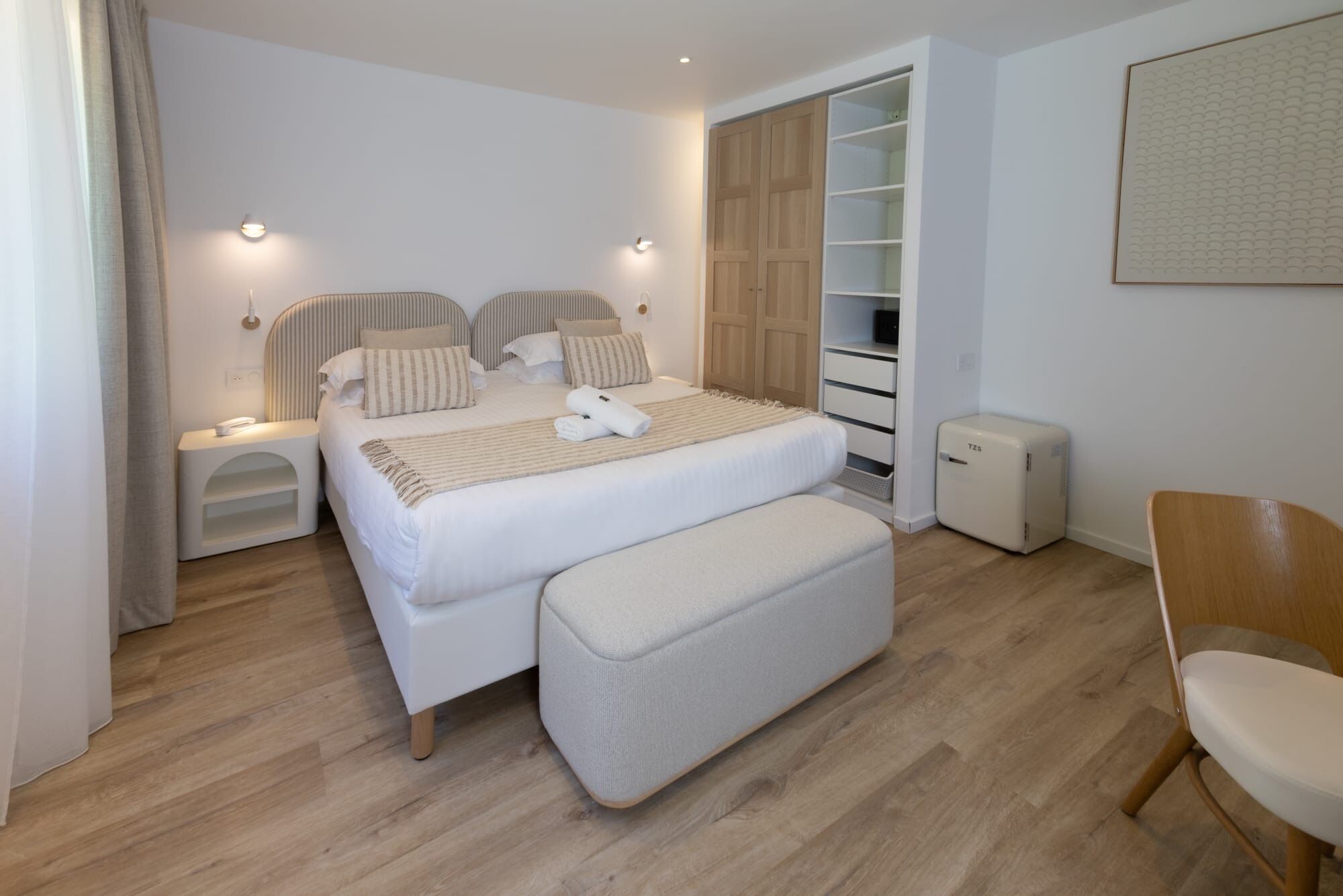 Un dormitorio moderno con cama, mesitas de noche, un banco, un armario y una silla.