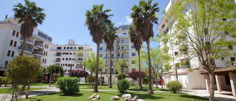 Un patio con palmeras, un césped con rocas y edificios blancos con balcones.
