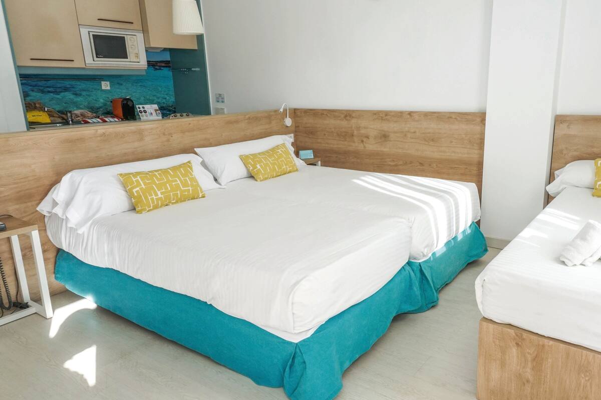 Een hotelkamer met twee bedden, elk met witte lakens en geel gestreepte kussens. De kamer heeft houten hoofdeinden en een turquoise bedrok.