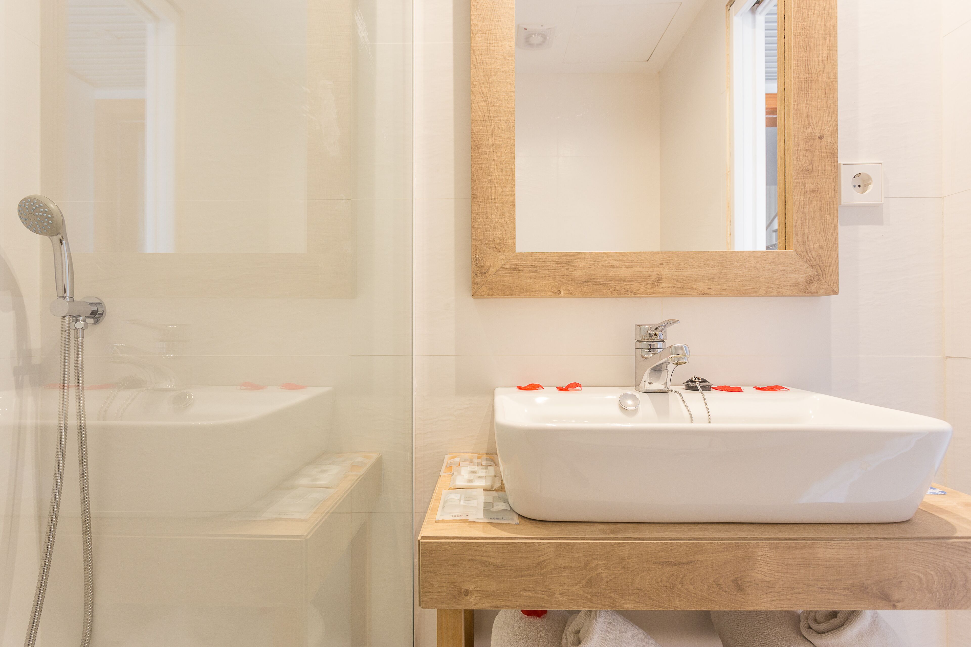Une salle de bain avec une douche à parois de verre, un lavabo blanc avec un meuble-vasque en bois et un miroir avec un cadre en bois.
