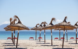 A beach with thatched umbrellas and red lounge chairs. - Caprice Tamarindos Apartments (Alcúdia)