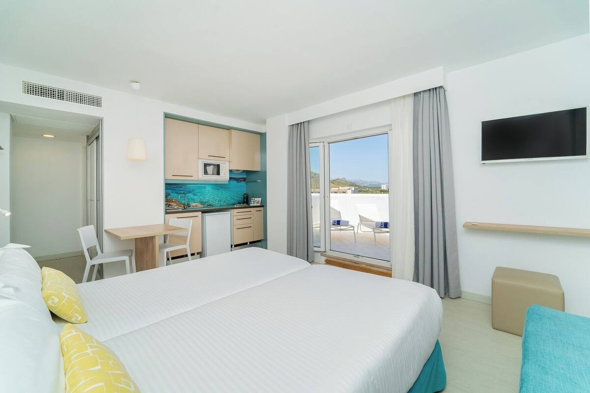 Hotelkamer met een bed, een bureau, een kitchenette en een balkon met uitzicht.