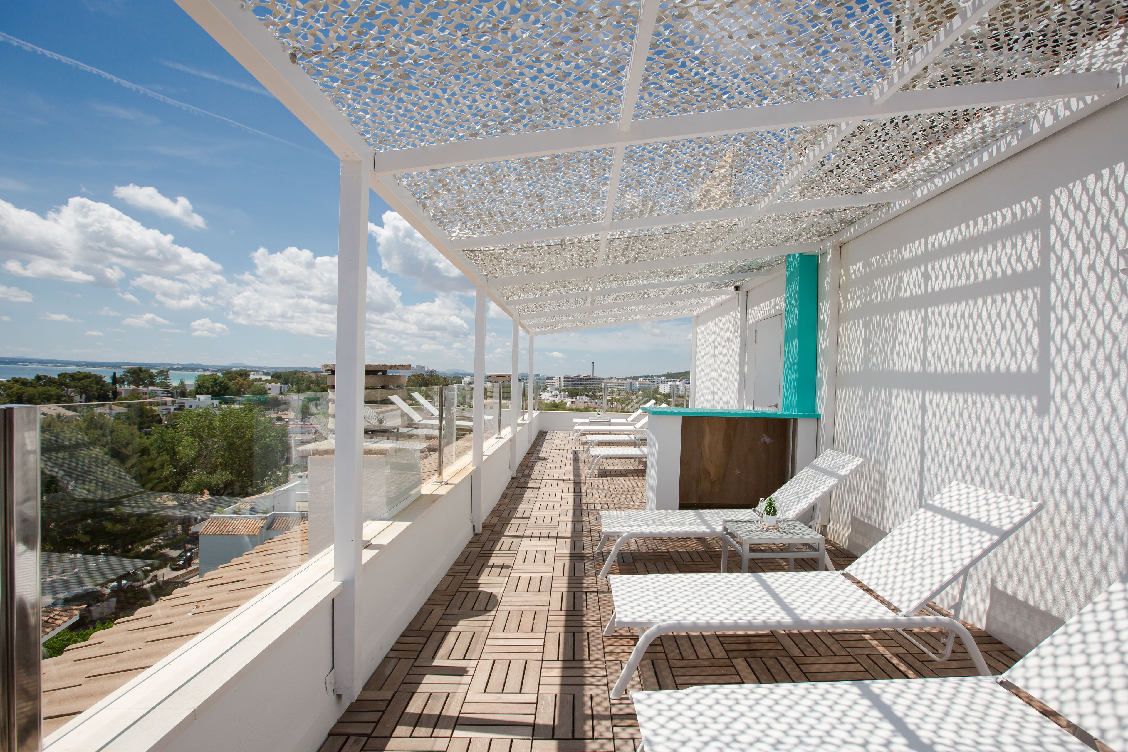 A balcony with white lattice ceiling, wooden flooring, and white lounge chairs.