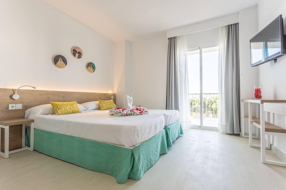 Een hotelkamer met een groot bed, een bureau, een televisie en een balkon met gordijnen.