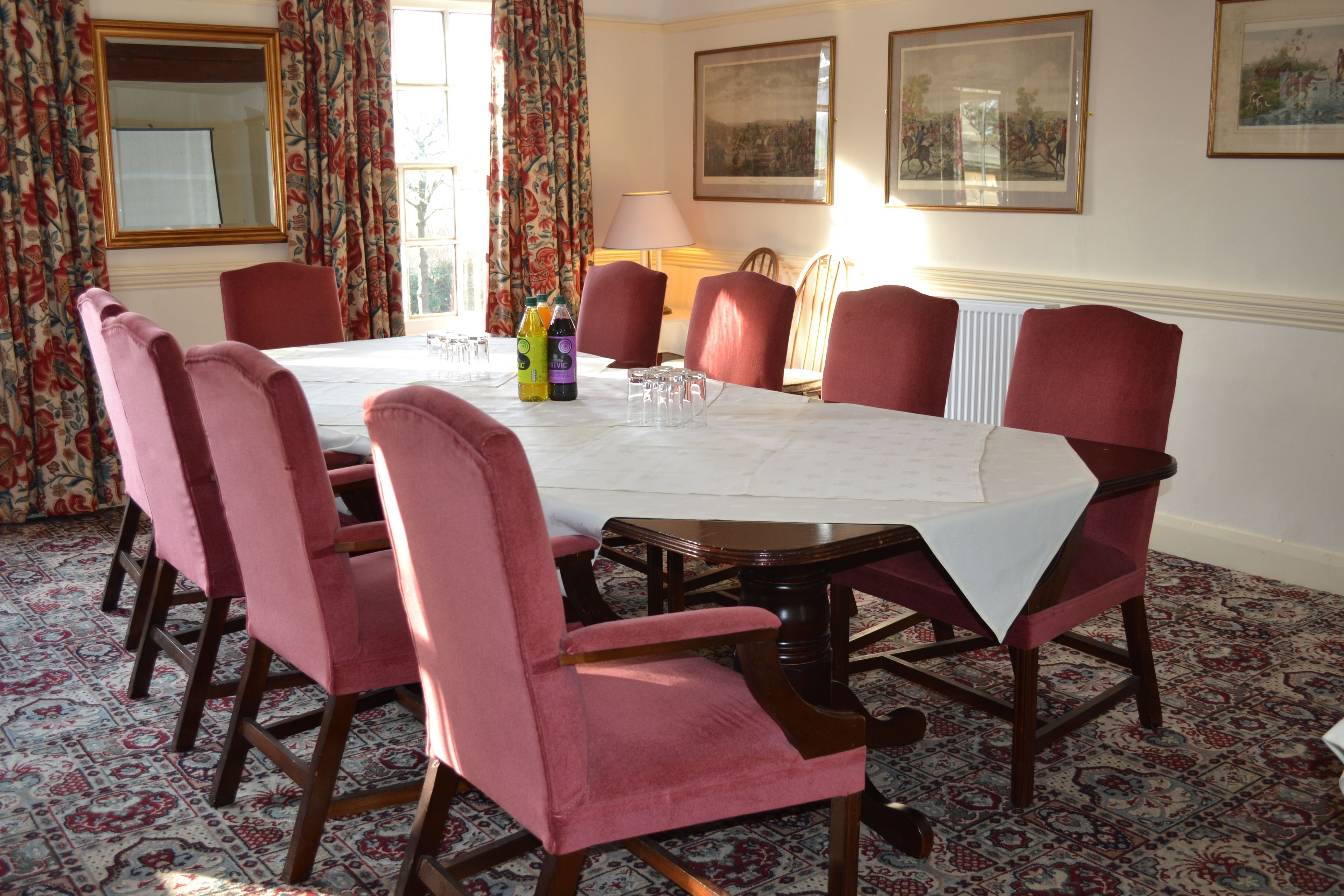 Una sala da pranzo con un tavolo rotondo, sedie imbottite rosse e un tappeto decorato.