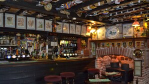 A bar area with a brick fireplace, wooden furniture, and a variety of bottles and glasses on shelves.