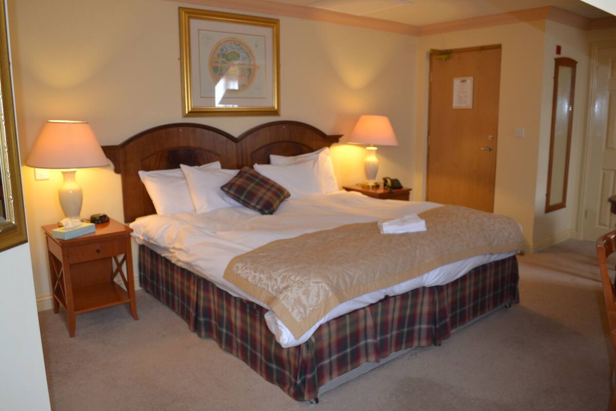A neatly made bed with a plaid bed skirt, two bedside tables with lamps, and a framed picture on the wall.