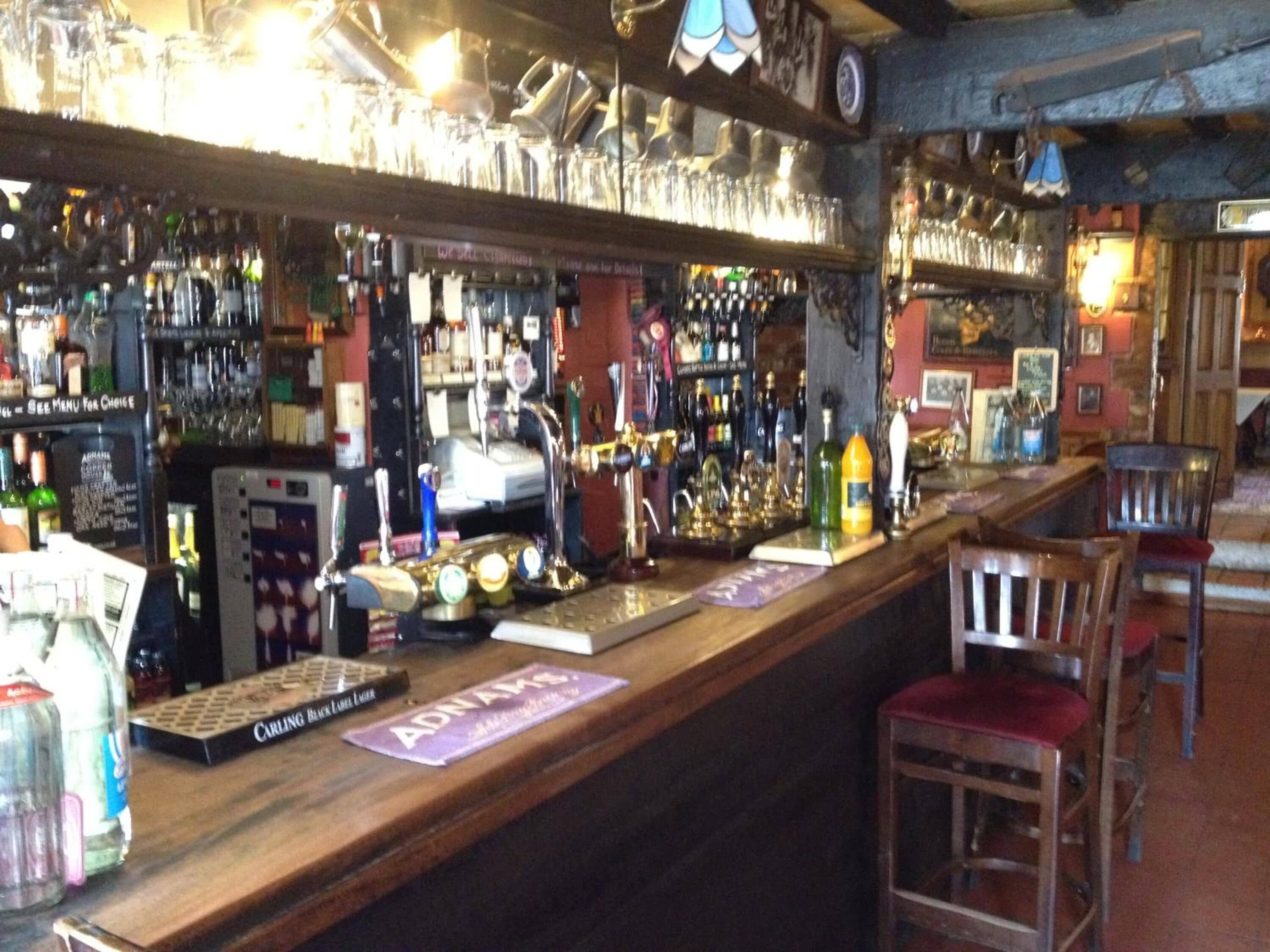 Un bar con mostrador de madera, varias botellas, vasos y una caja registradora.