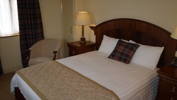 A neatly made bed with a plaid pillow, a bedside lamp, and a chair in a hotel room.