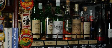 Bar con diversas botellas de alcohol, incluyendo whisky y vino, y una selección de guías de cerveza.