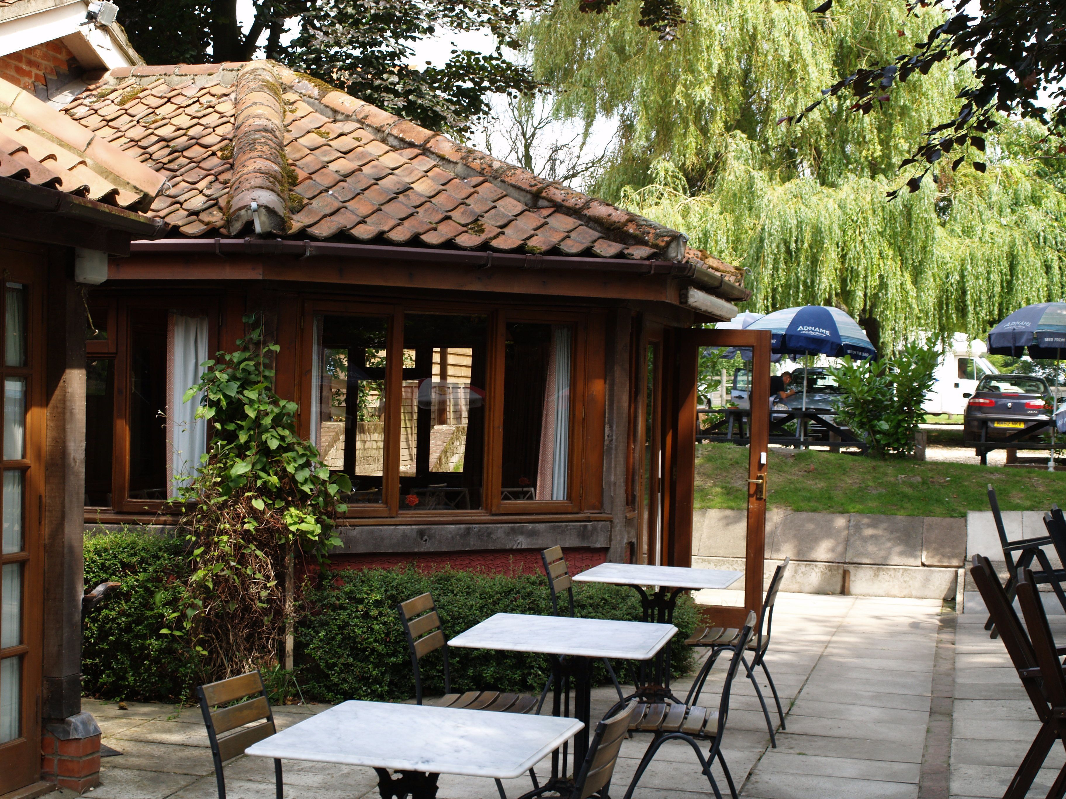 Un restaurante con terraza, tejado de baldosas y vistas a coches aparcados y árboles.