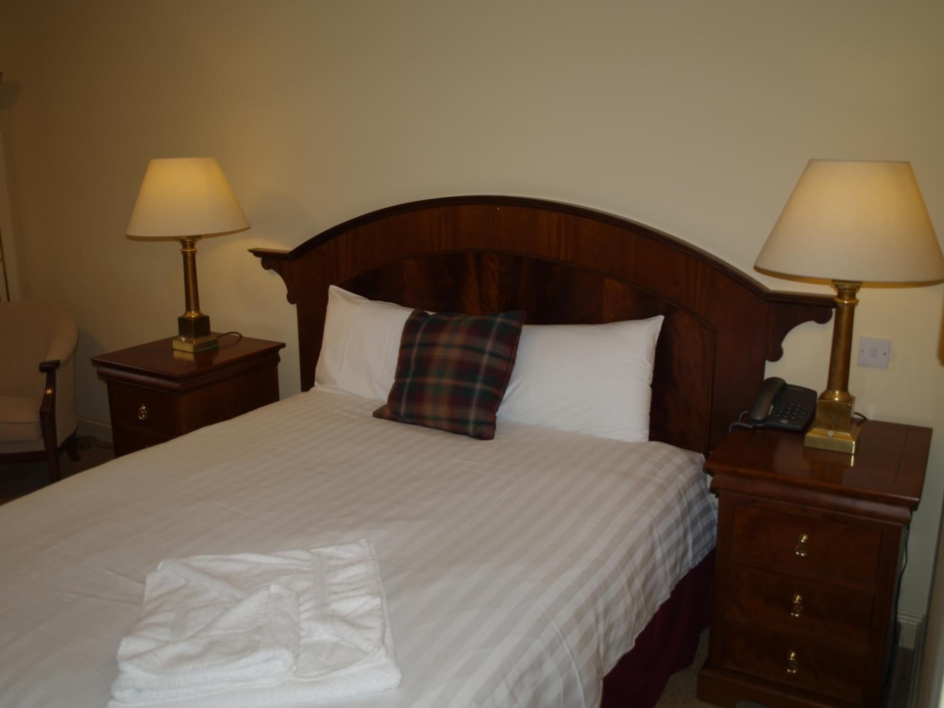 A neatly made bed with a plaid pillow, two bedside tables with lamps, and a chair.
