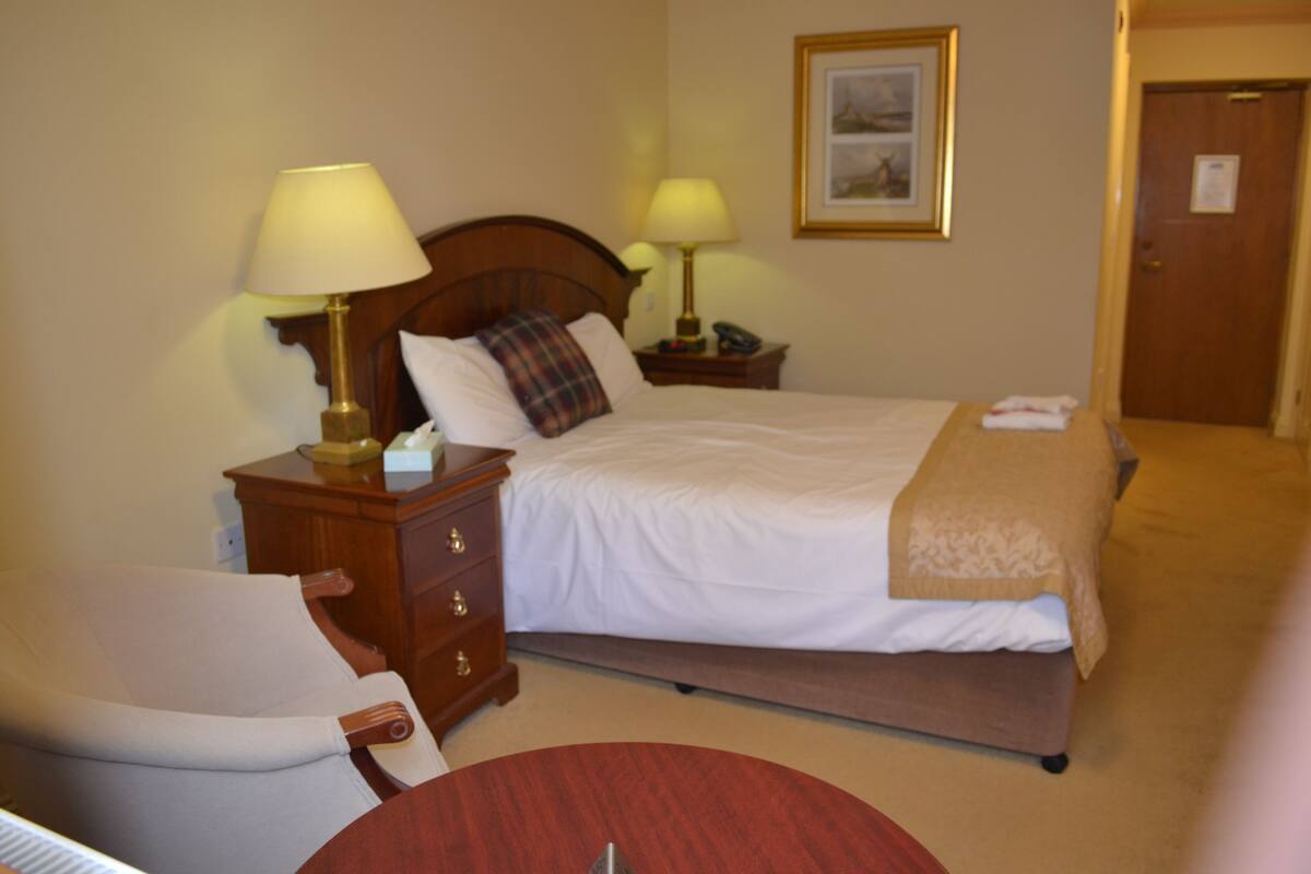 A hotel room with a bed, two bedside tables with lamps, a chair, and a door.