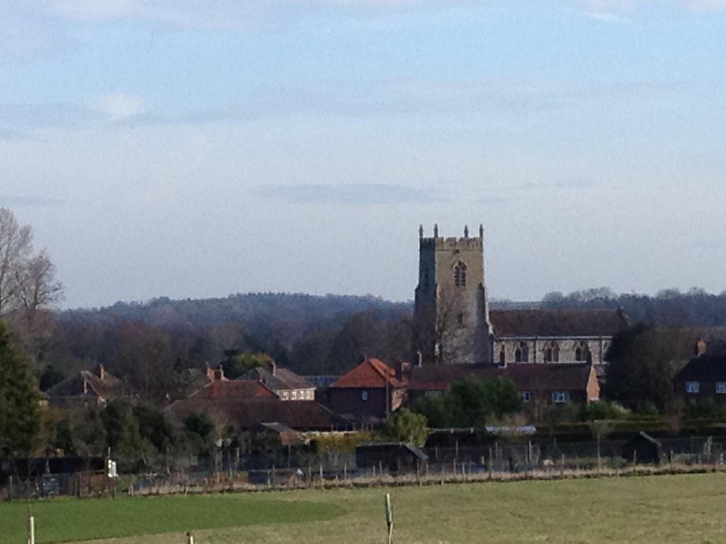 A church with a tall tower, surrounded by residential houses and a fenced field.