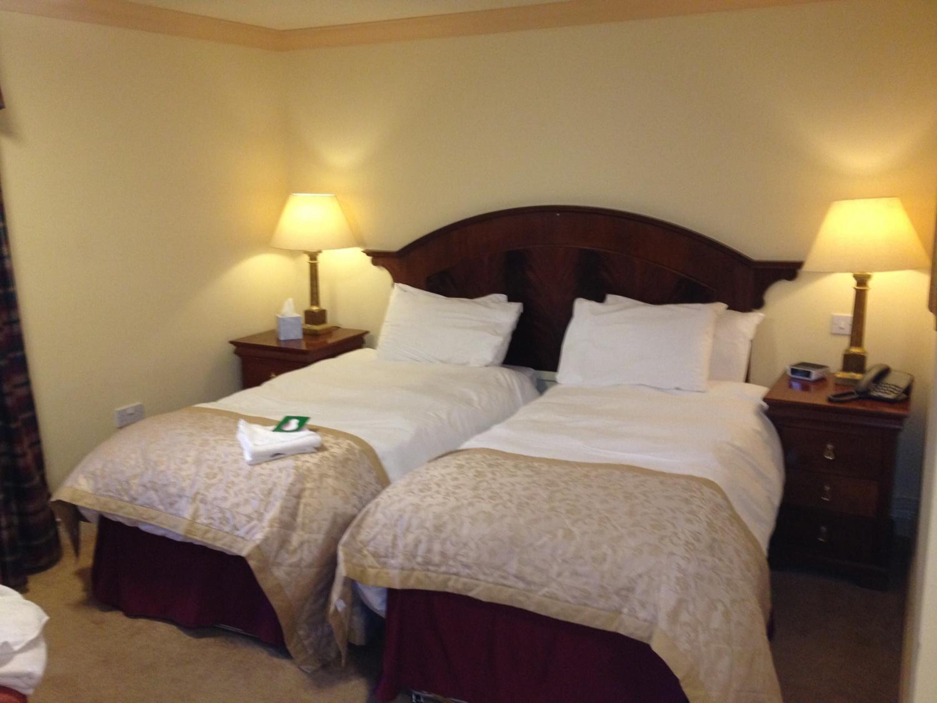 A hotel room with two beds, each with a matching nightstand, a lamp, and a telephone.