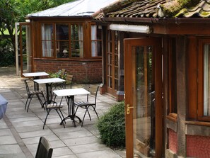 Een terras met tafels en stoelen, een bakstenen muur en een houten deur.
