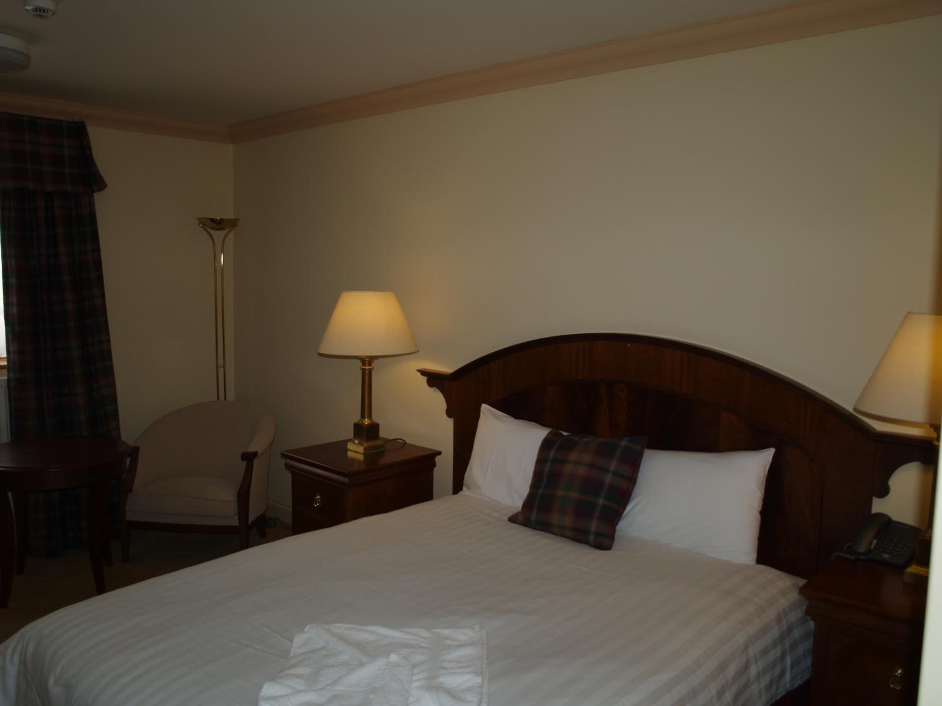 A hotel room with a large bed, two bedside tables with lamps, a chair, and a desk.