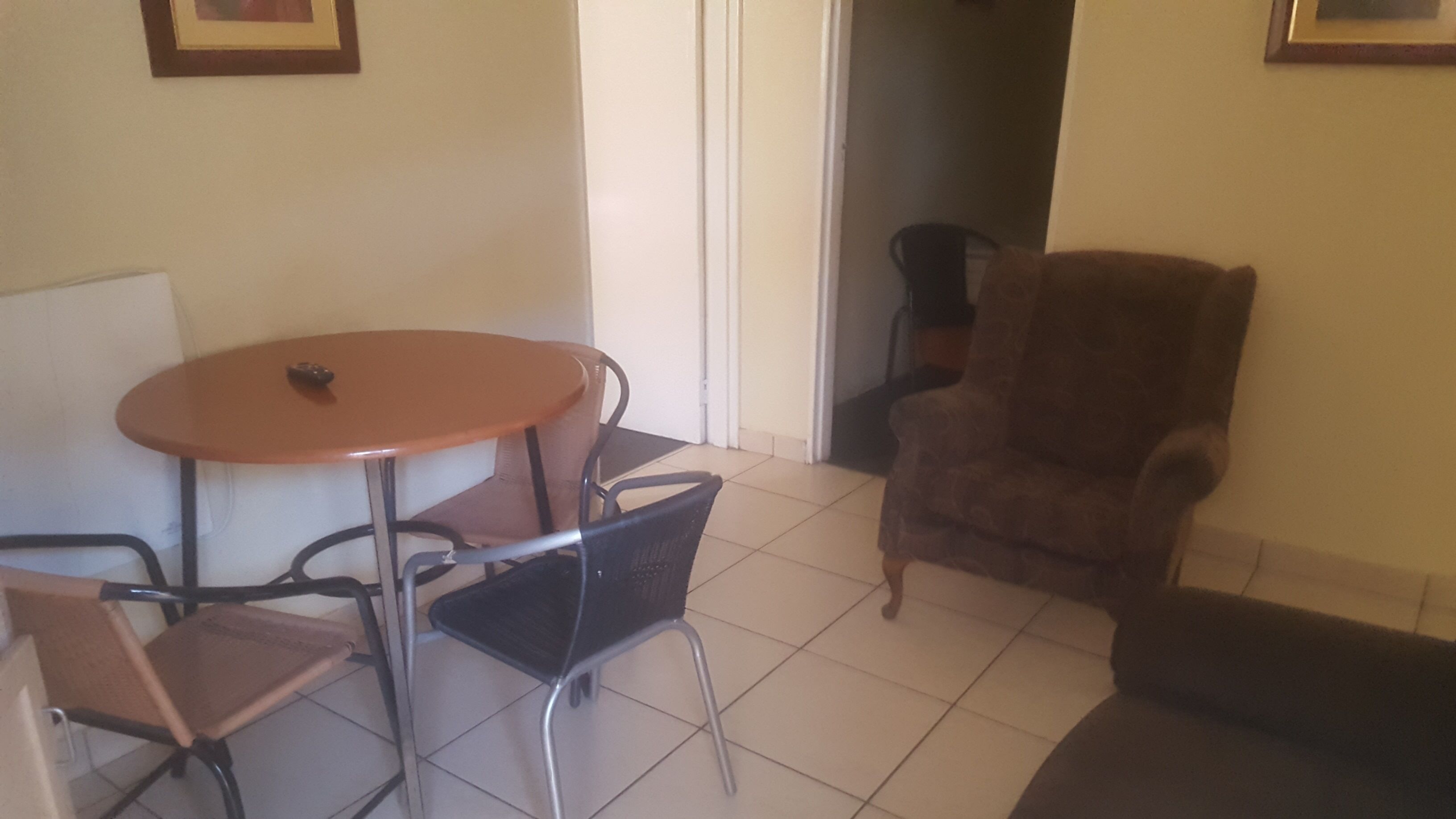 A small room with a round table and four chairs, a brown armchair, and a sofa.