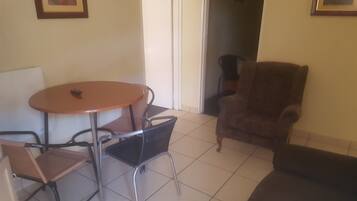 A small room with a round table and four chairs, a brown armchair, and a sofa.