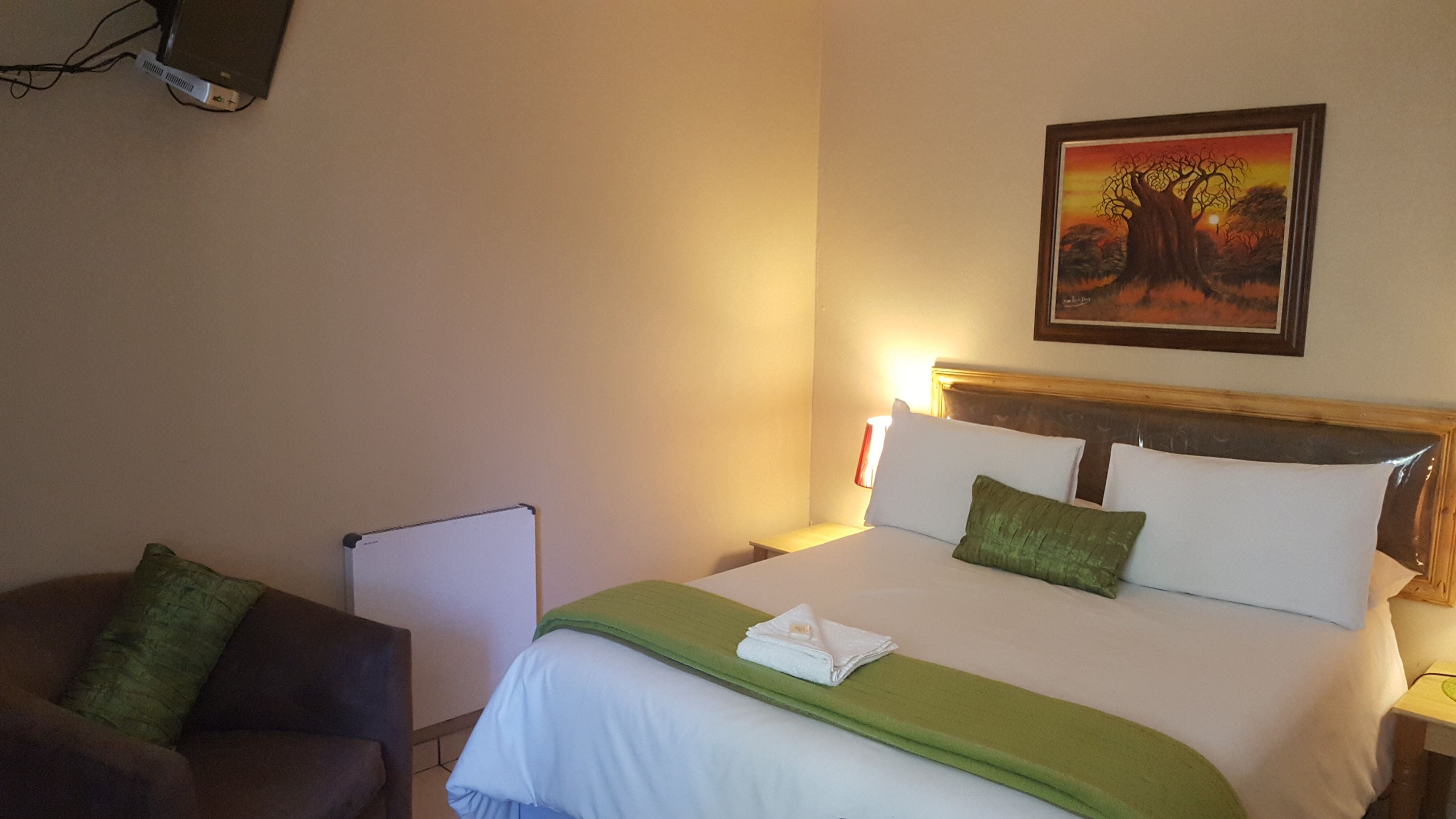 A hotel room with a bed, a chair, a desk, and a painting on the wall.