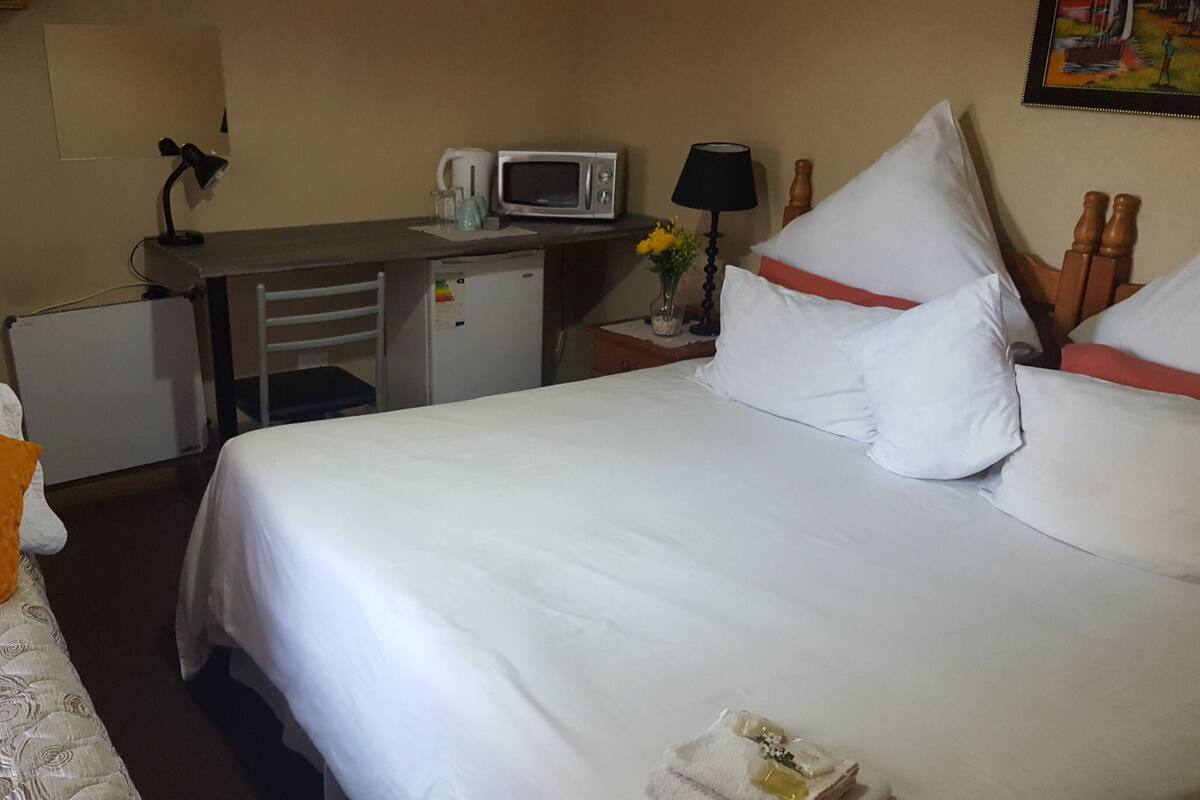 Ein Hotelzimmer mit einem Bett, einem Schreibtisch mit einer Mikrowelle, einer Lampe und einem kleinen Tisch mit Blumen.
