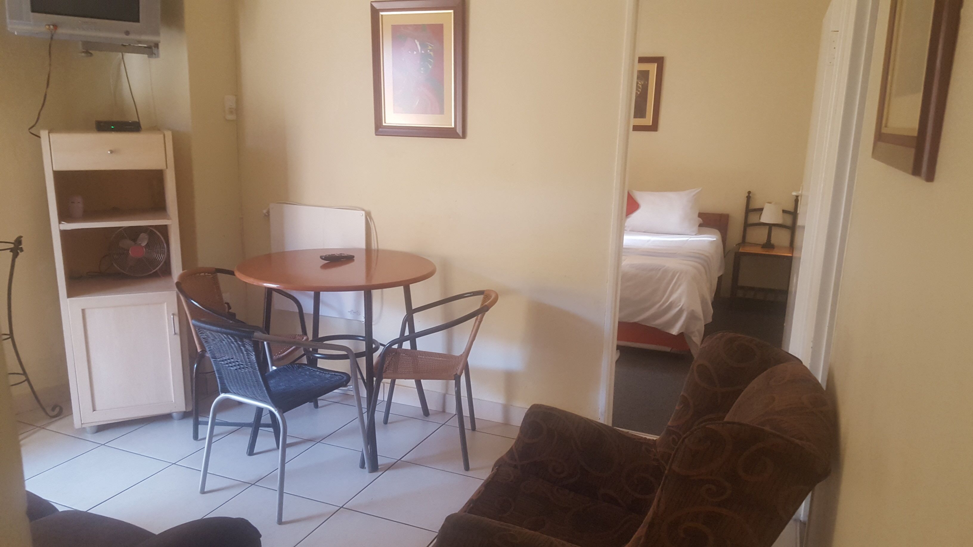 A room with a dining table, two chairs, a bed, and a TV mounted on the wall.