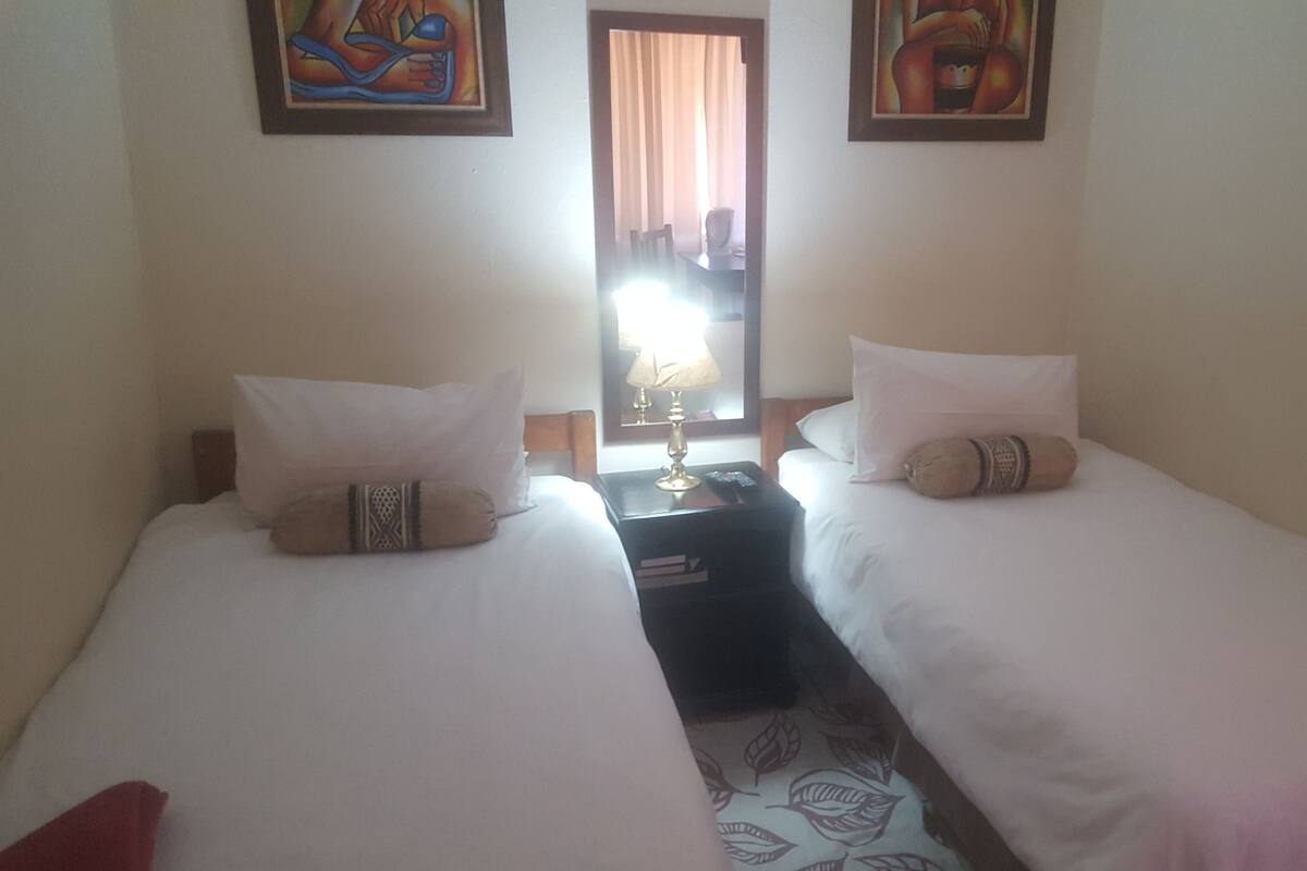 Ein Hotelzimmer mit zwei Einzelbetten, einem Nachttisch mit Lampe und Bildern an den Wänden.