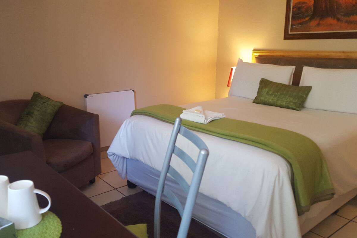 Ein Hotelzimmer mit Bett, Stuhl, Schreibtisch mit Tasse und einem Bild an der Wand.