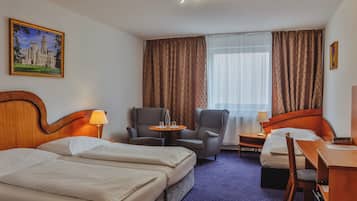 A hotel room with two beds, a desk, a chair, a small table, and a window with curtains.