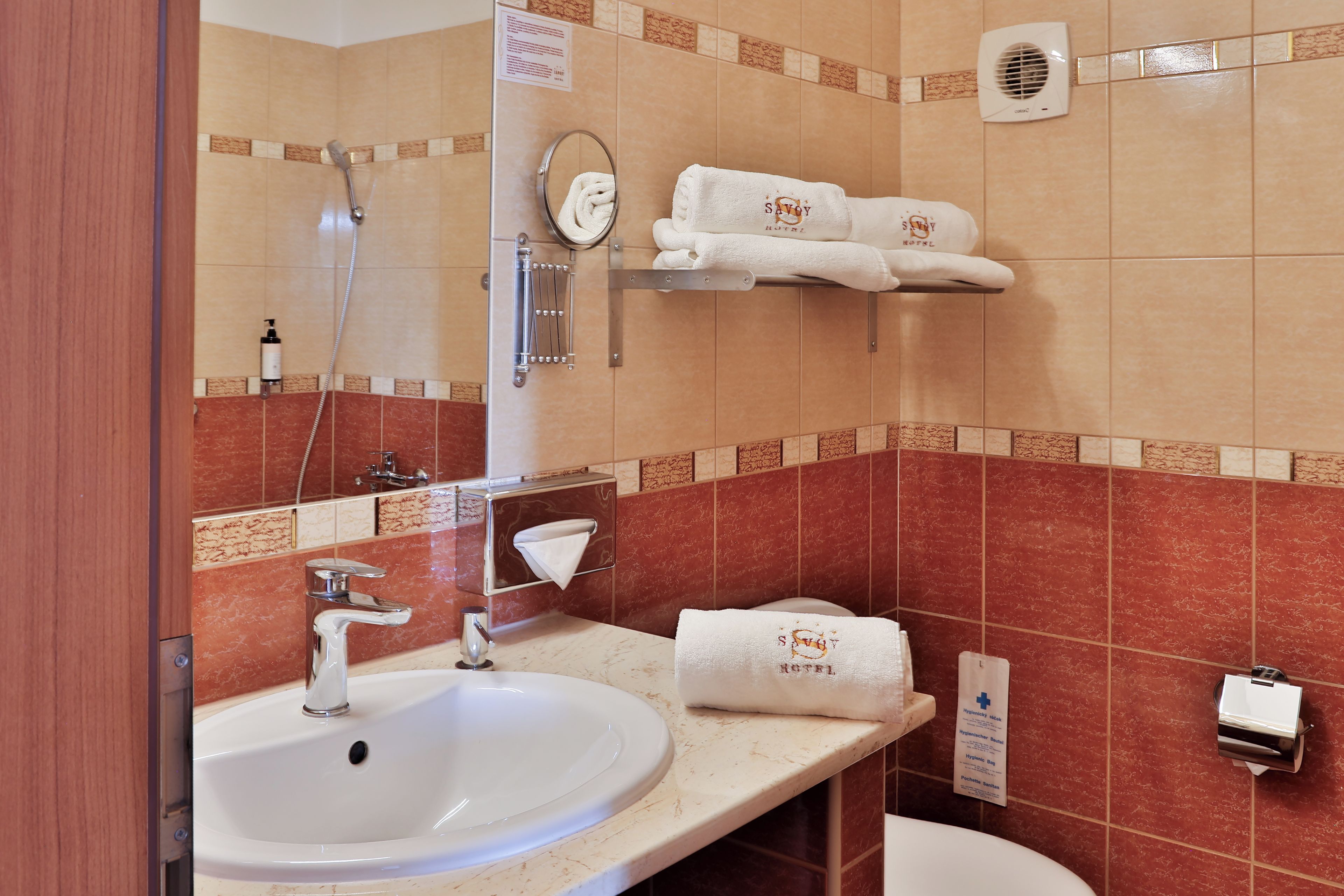A hotel bathroom with a sink, mirror, towel rack, and a hand dryer.