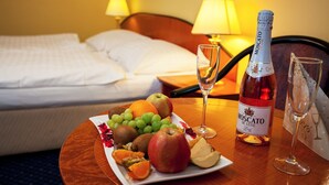 A hotel room with a bed, a bedside table with a bottle of Moscato de Luxe wine, a glass, and a plate of fruit. - Savoy (Ceske Budejovice)