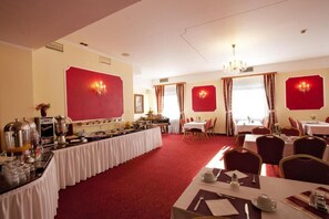 A hotel dining area with a long buffet table, multiple dining tables, and red wall decorations.