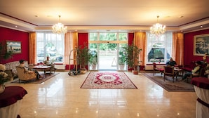 A spacious lobby with a red and white color scheme, featuring a large chandelier, potted plants, and a central area with a red carpet. - Savoy (Ceske Budejovice)