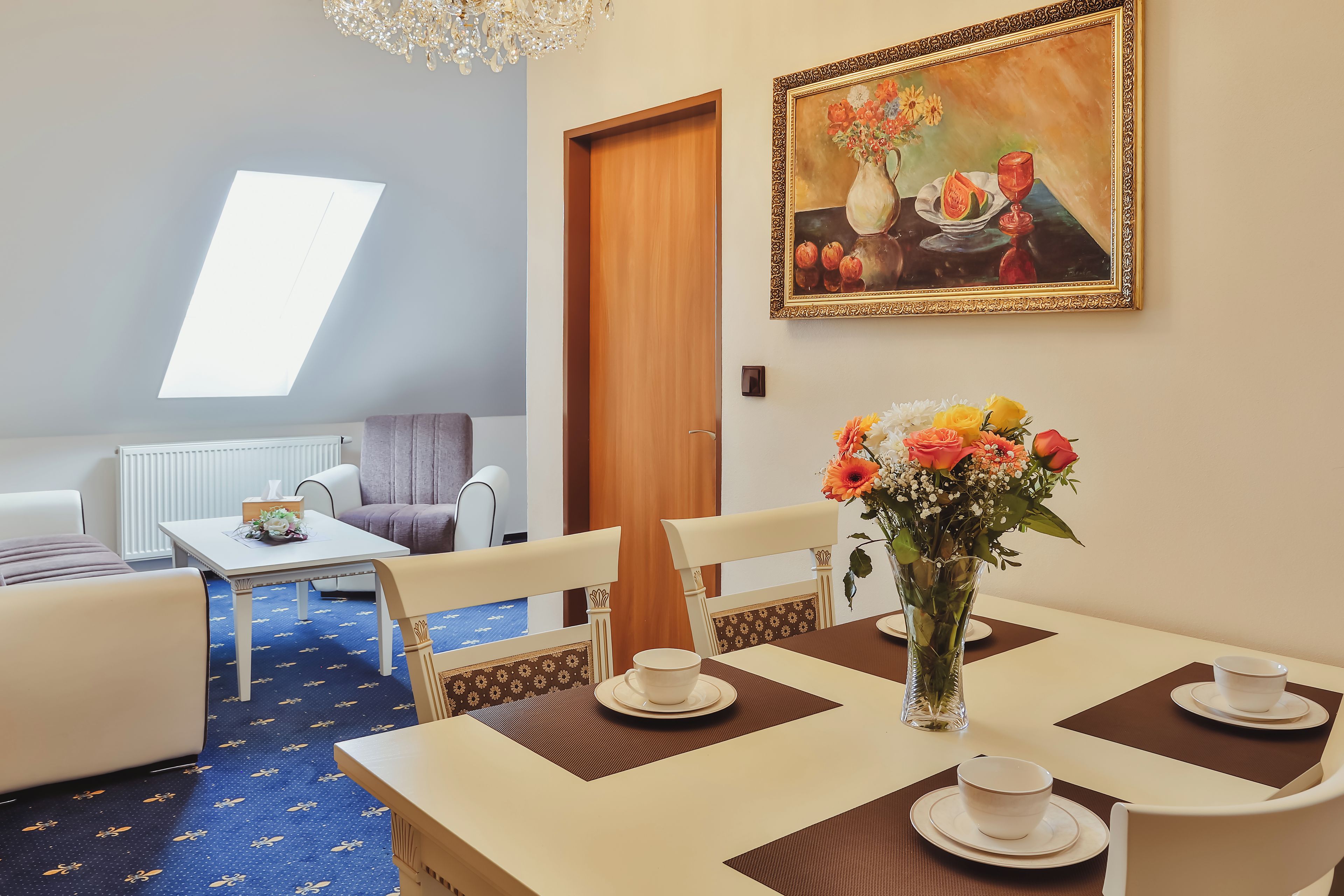 A dining area with a table set for two, a vase of flowers, and a painting on the wall.