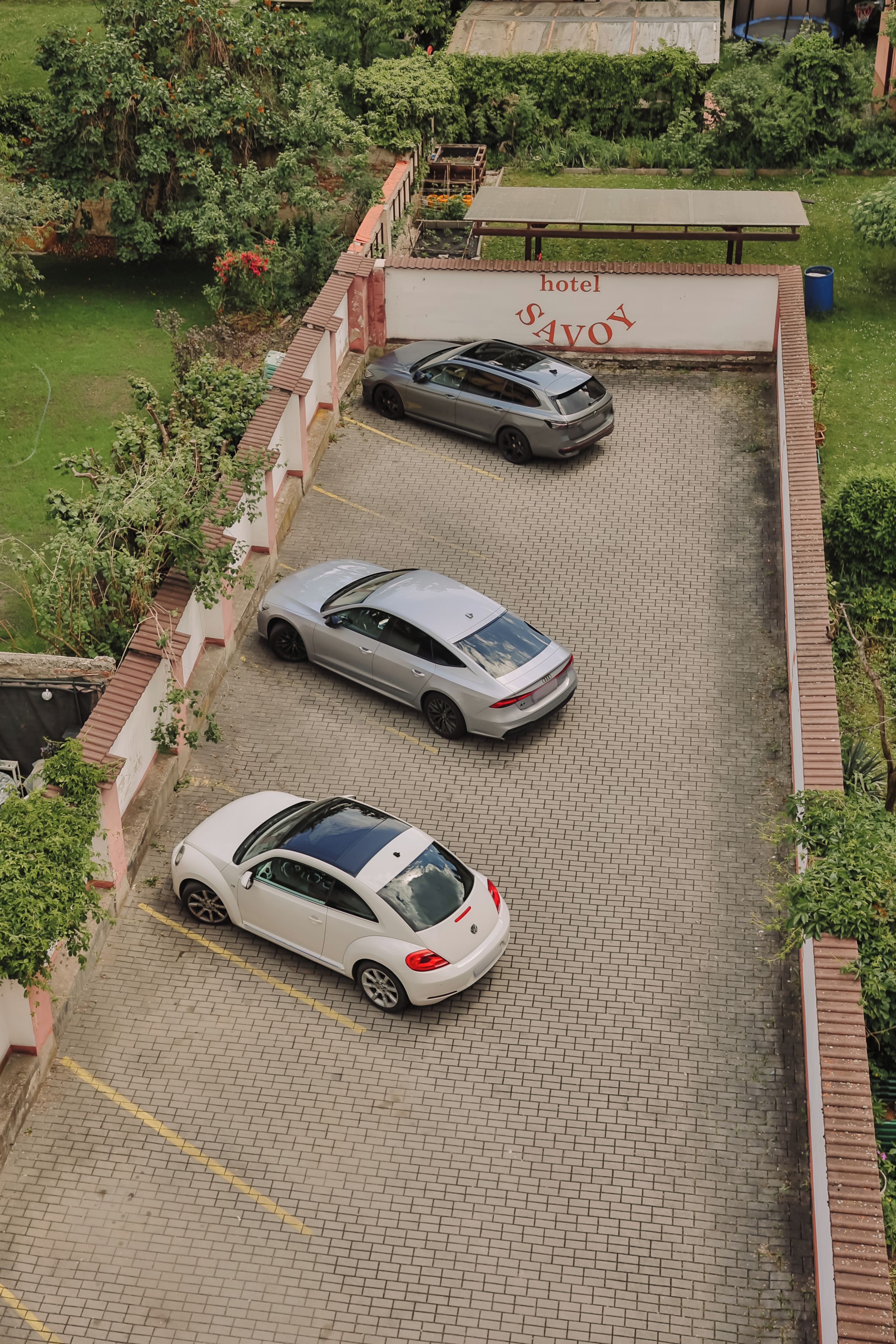 A parking area with three cars, a garden, and a building with a sign.