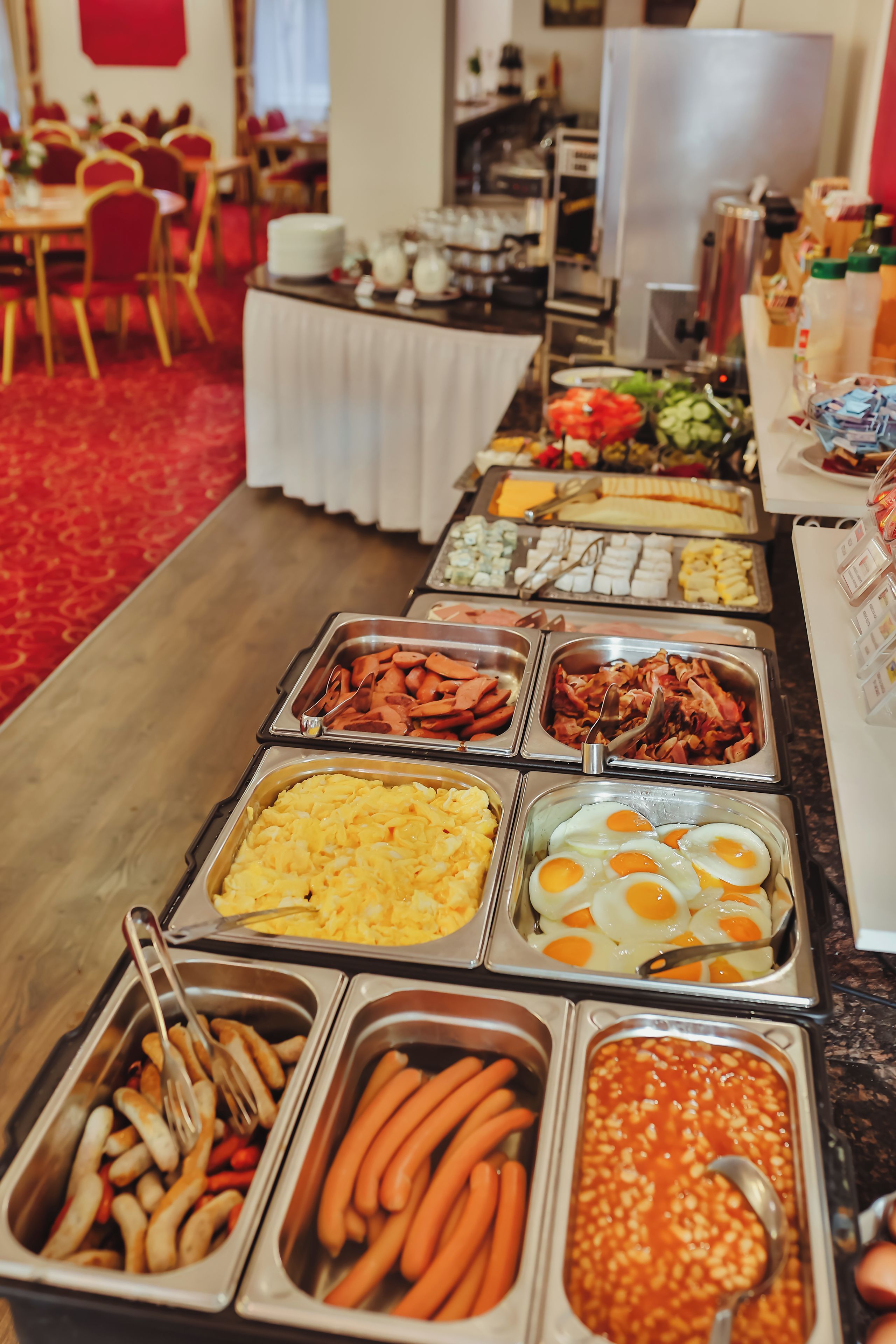 A buffet with various food options including eggs, sausages, and vegetables.