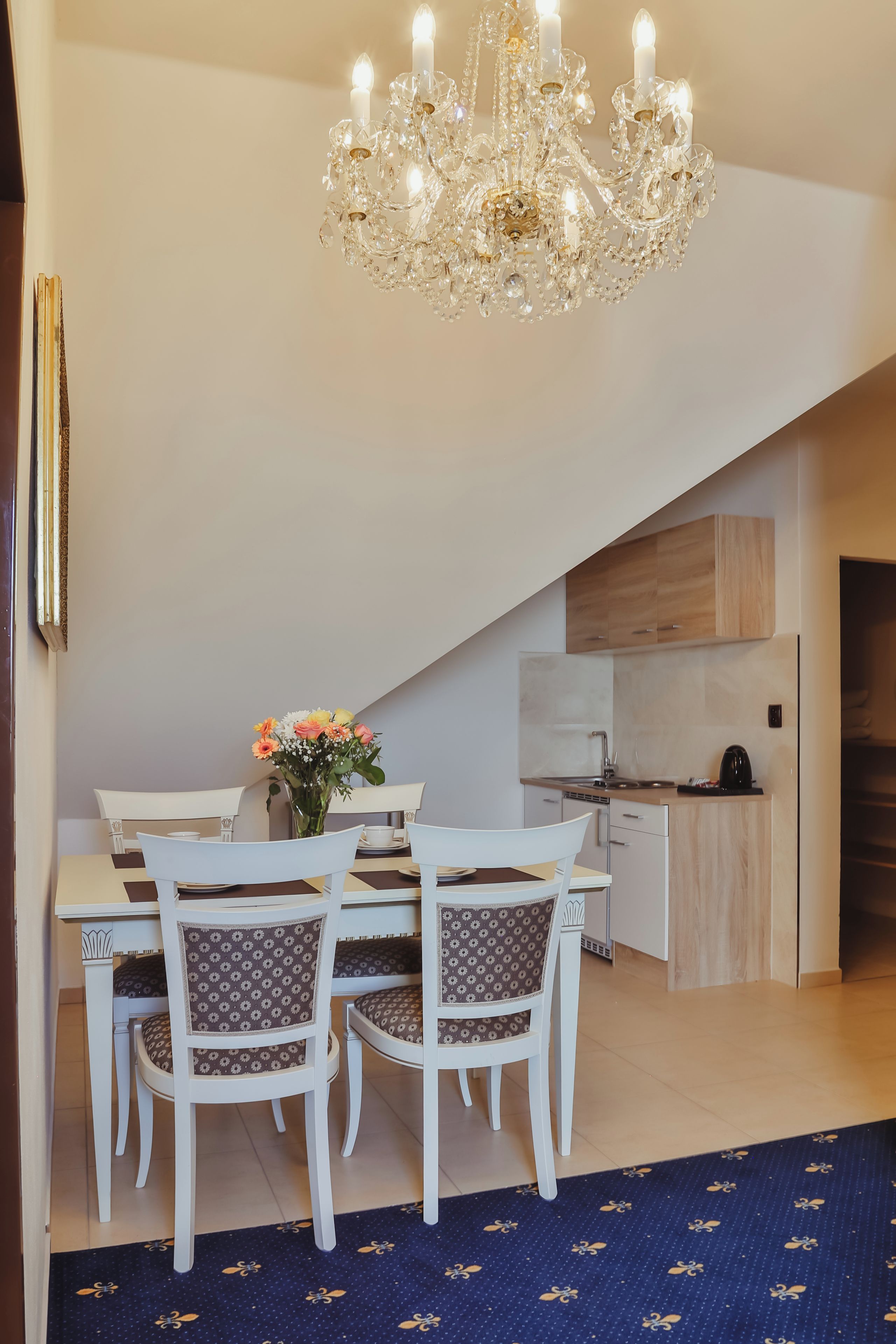 A dining area with a chandelier, white chairs, a table, and a vase with flowers.