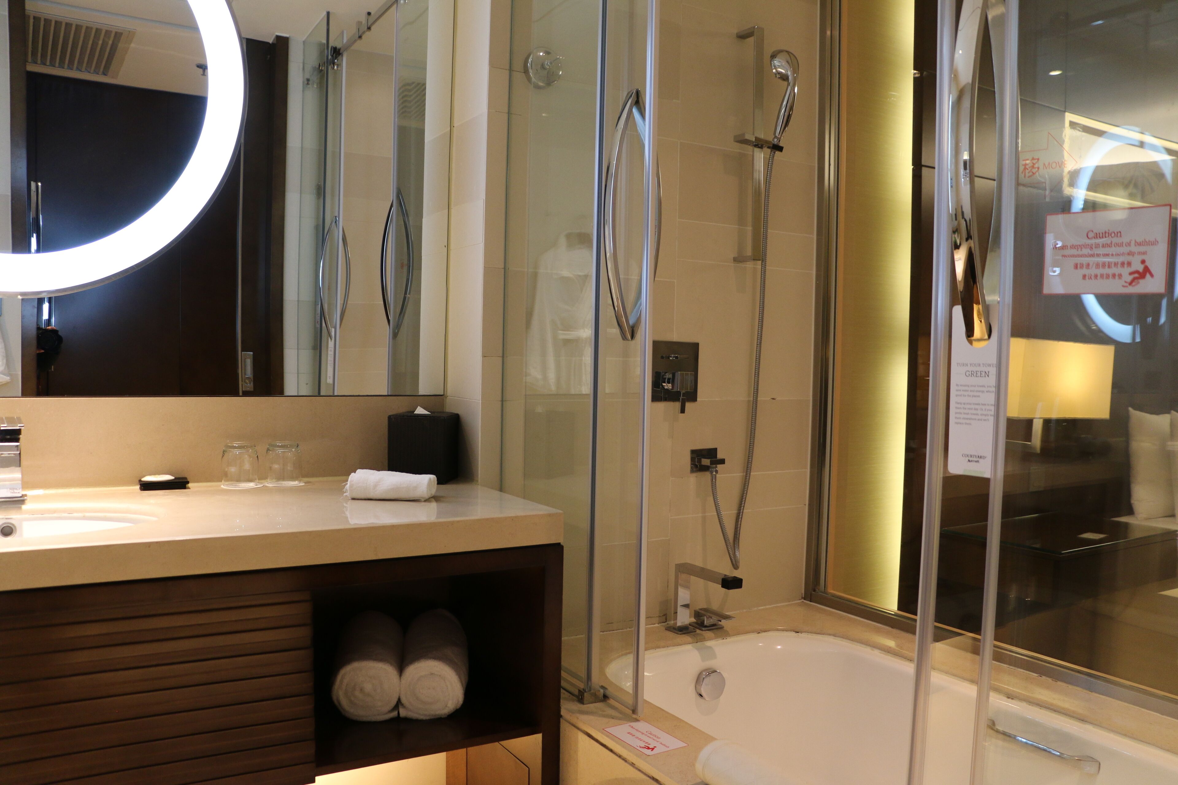 Un baño moderno con ducha de vidrio, un espejo redondo y una bañera.