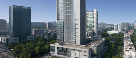 Un hotel moderno de gran altura con una fachada de vidrio llamativa, rodeado de espacios verdes urbanos y otros edificios.