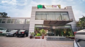 A modern hotel with a large glass facade, a sign reading "Hotel One," and a parking lot with several cars. - Hotel One The Mall Lahore (Lahore)