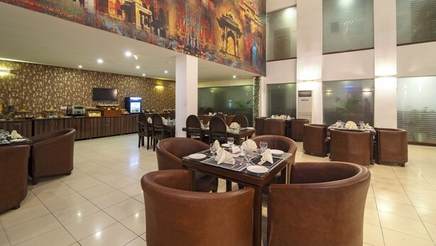 A spacious hotel lobby with a large mural, multiple dining tables, and comfortable seating areas. - Hotel One The Mall Lahore (Lahore)