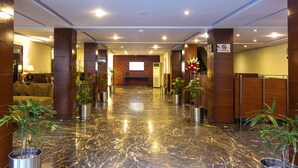 A lobby with a marble floor, wooden columns, a sofa, and potted plants. - Hotel One The Mall Lahore (Lahore)
