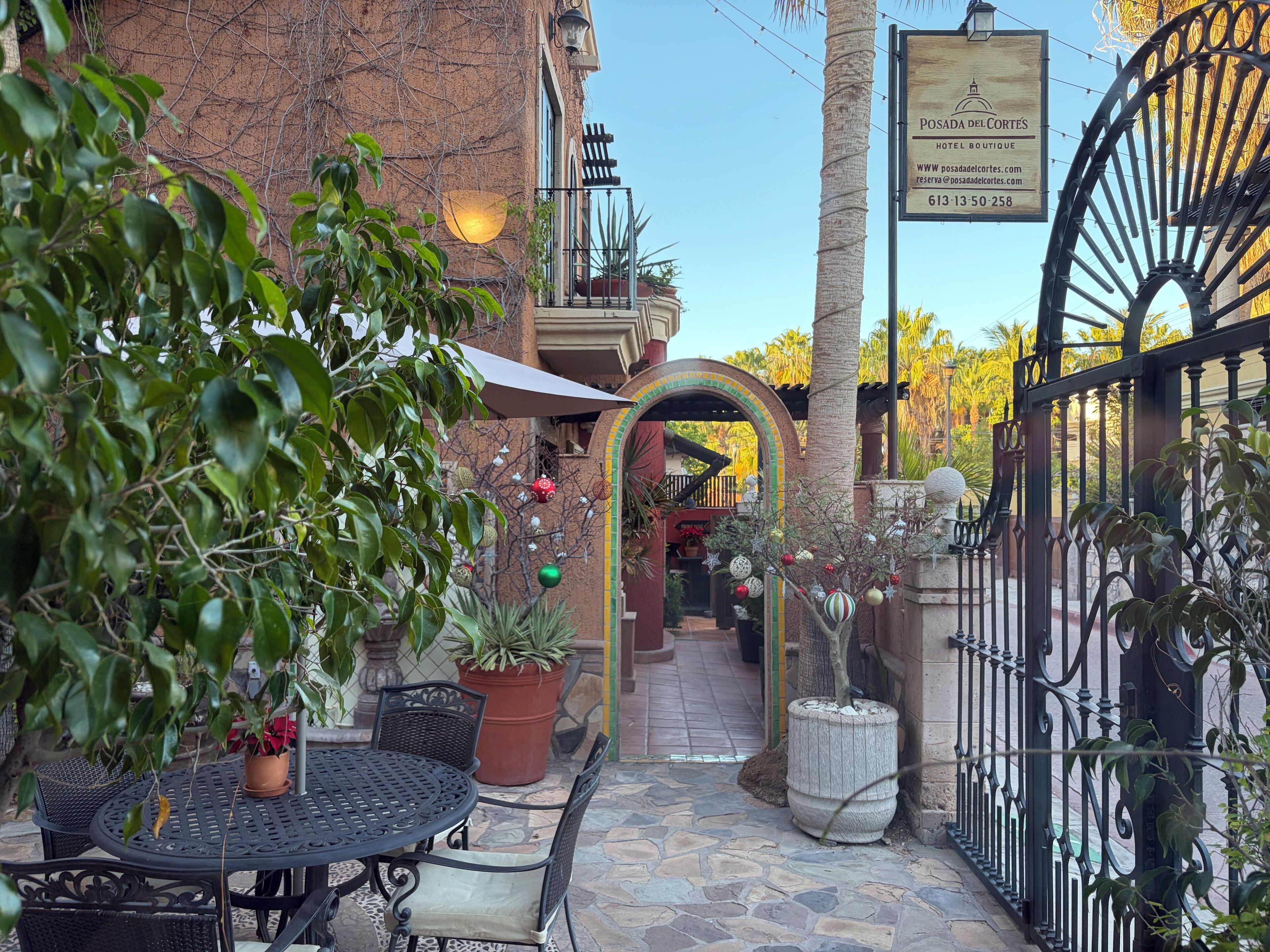 Un patio con una mesa redonda y sillas, una planta en maceta y un letrero para el Hotel Boutique Posada del Cortes.