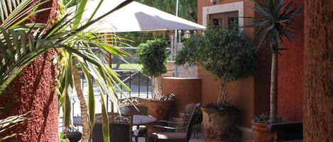 An outdoor patio area with a table and chairs, surrounded by potted plants and a white umbrella.